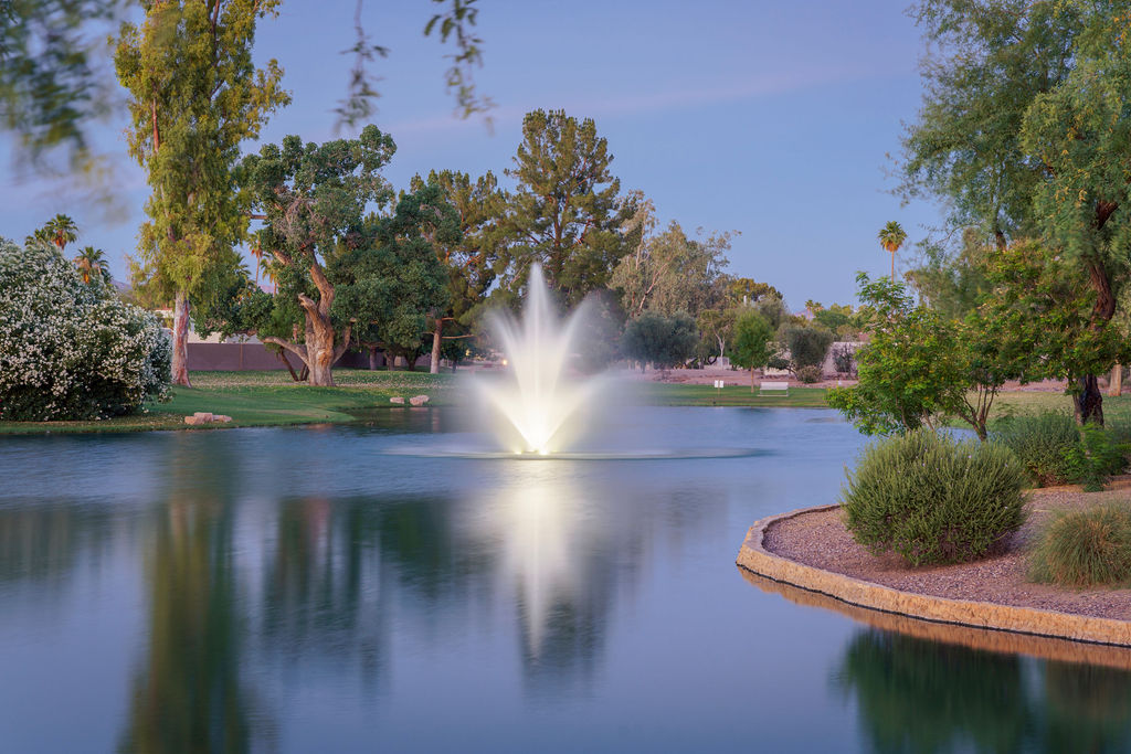 An illuminated fountain reflected in a McCormick Ranch lake, surrounded by trees and landscaped banks